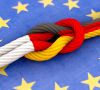 Ein Knoten in einem Seil in den Landesfarben von Deutschland und Frankreich. Der Untergrund ist eine Europaflagge.