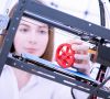 Frau an 3D-Drucker mit additiv gefertigtem Zahnrad aus Kunststoff