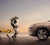 Zwei Roboter von Boston Dynamics stehen einem Hyundai-Fahrzeug gegenüber.