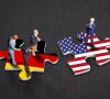 Zwei Puzzleteile, das eine in der Flagge Deutschlands, das andere in der der USA. Auf dem USA-Puzzle steht eine Figur, die wie Donald Trump aussieht. Auf der deutschen stehen drei Menschen.