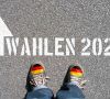 Zwei Schuhe mit Deutschlandflaggen. Auf dem Boden steht ein Pfeil und "Wahlen 2021".