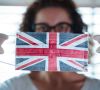 Eine Frau zeigt eine Maske, auf die die Flagge Großbritanniens aufgedruckt ist.