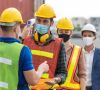 Mitarbeitern mit Schutzhelm und Maske wird Fieber gemessen