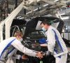 Zwei Volkswagen-Mitarbeiter arbeiten mit Mundschutz an einem Auto.