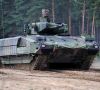 Ein Schützenpanzer Puma der Bundeswehr fährt durch sandiges Gelände, im Hintergrund ist ein Wald zu sehen.