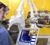 Ein Arbeiter schaut in einem Werk auf einen Bildschirm, der an einen Roboter angeschlossen ist.