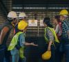 Mitarbeiter, die Arbeitskleideung wie gelb leuchtende Westen und Helme tragen, schauen ungläubig auf ein Schild, auf dem "Shutdown" steht.