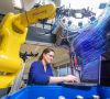 Eine Bosch-Mitarbeiterin schaut auf einen Laptop, daneben ein Roboterarm.