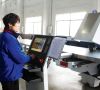 Chinesicher Arbeiter mit blauer Jacke bedient Computer in Werkshalle