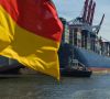 Containerschiff legt am Hafen an. Im Vordergrund weht eine Deutschlandflagge.