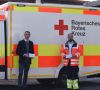 Stefan Waldeisen (links), Mitglied der Geschäftsfürung, übergibt einen Teil der Schutzmasken an Christian Haberkorn, Leiter des Rettungsdienstes beim Bayerischen Roten Kreuz. Die beiden stehen vor einem Rettungswagen.