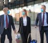 Zwei Geschäftsmänner und eine Geschäftsfrau, die alle Maske tragen, und Koffer mit sich haben, laufen nebeneinander