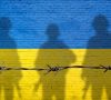Flagge der Ukraine, gemalt auf einer Backsteinmauer mit Soldatenschatten. 